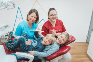 Kinderbehandlung: Kinder auf Stuhl mit Ärztin und Mitarbeiterin / Fotograf*in: ElsnerFotografie - Jessica Elsner